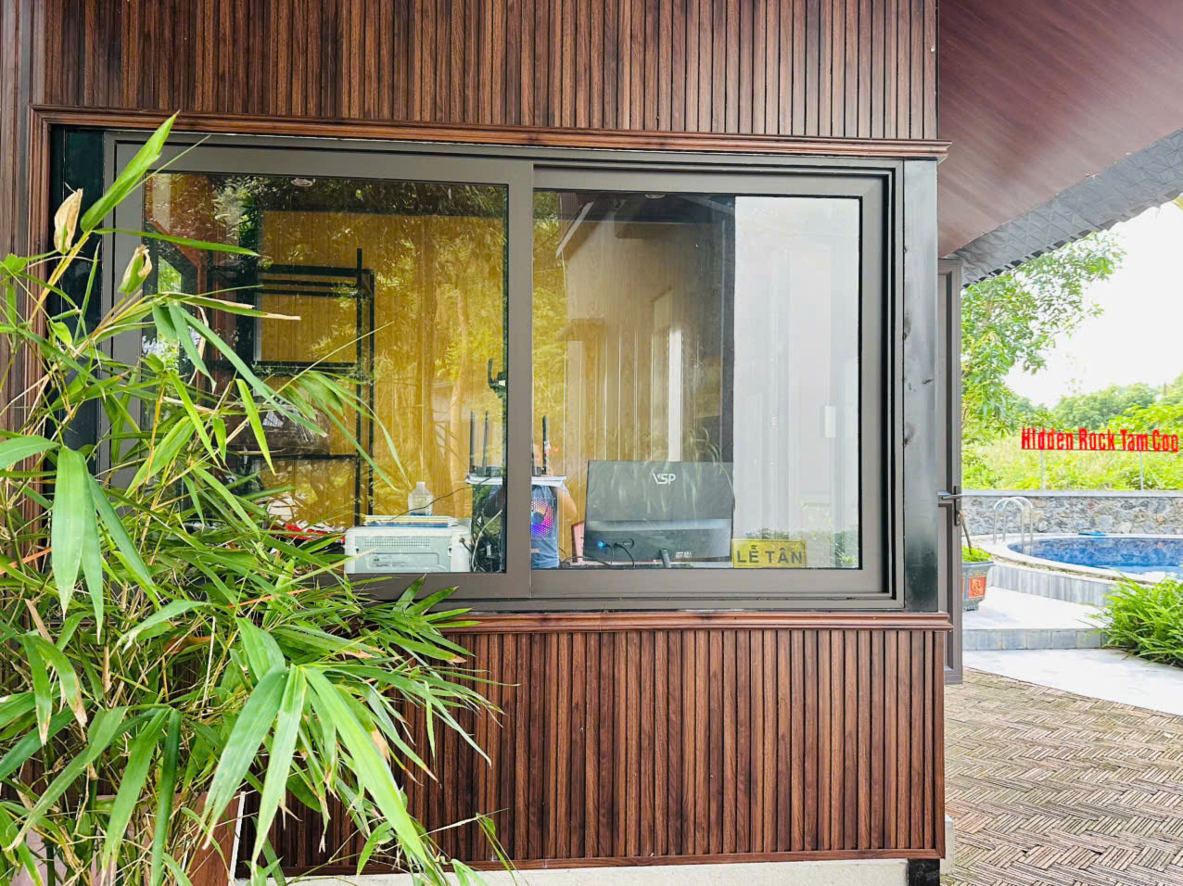 A modern building with a large window, wooden paneling, and a view of a swimming pool.