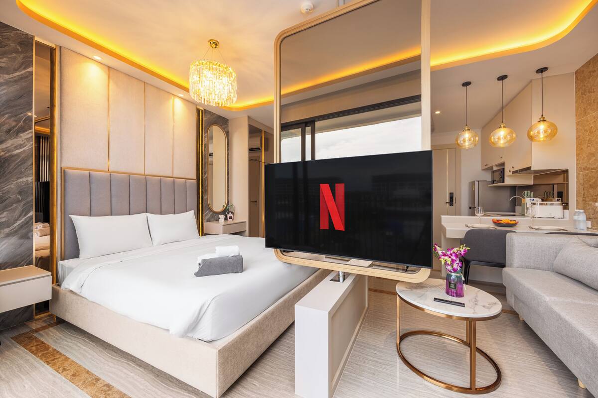 A modern hotel room with a large bed, a TV, a small table, and a sofa.