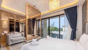A modern hotel room with a large bed, a sofa, a mirror, and a view of the outdoors. - Bellevue Lagoon Premium Apart Hotel (Choeng Thale)