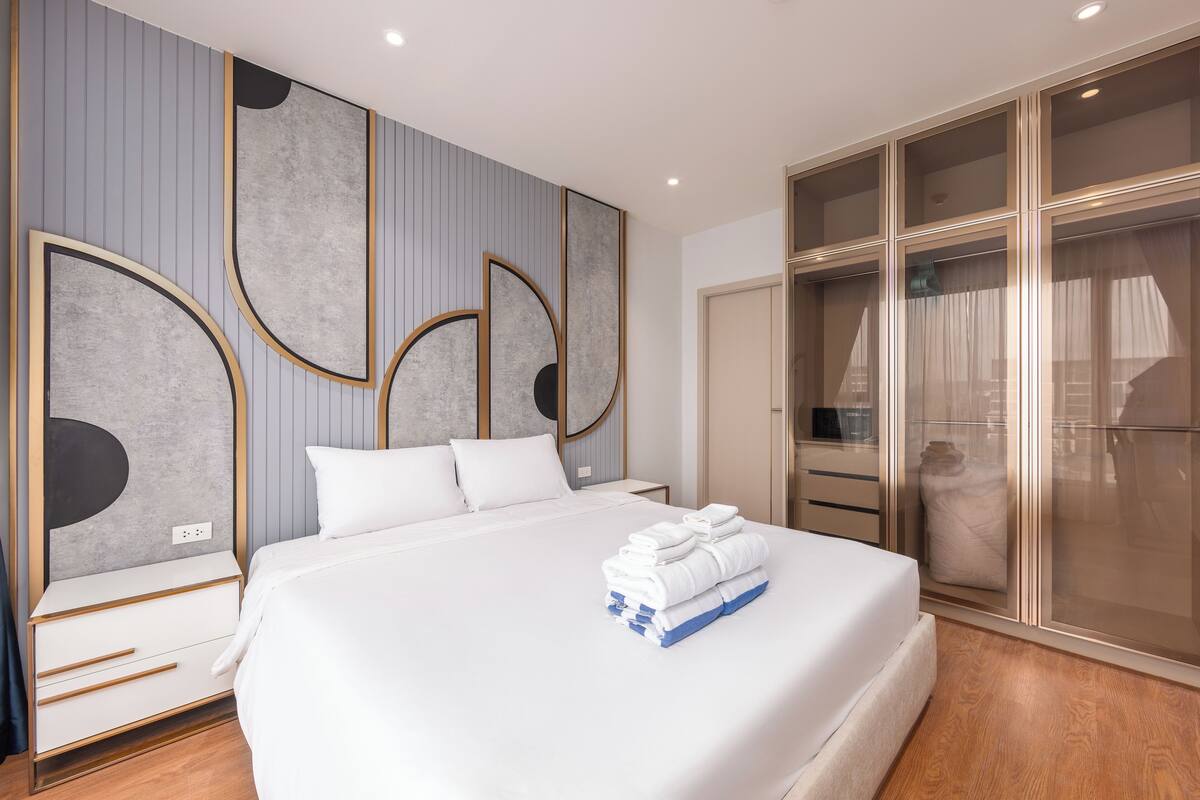 A modern hotel room with a large bed, a bedside table, a wardrobe with a mirror, and a wall with abstract art.