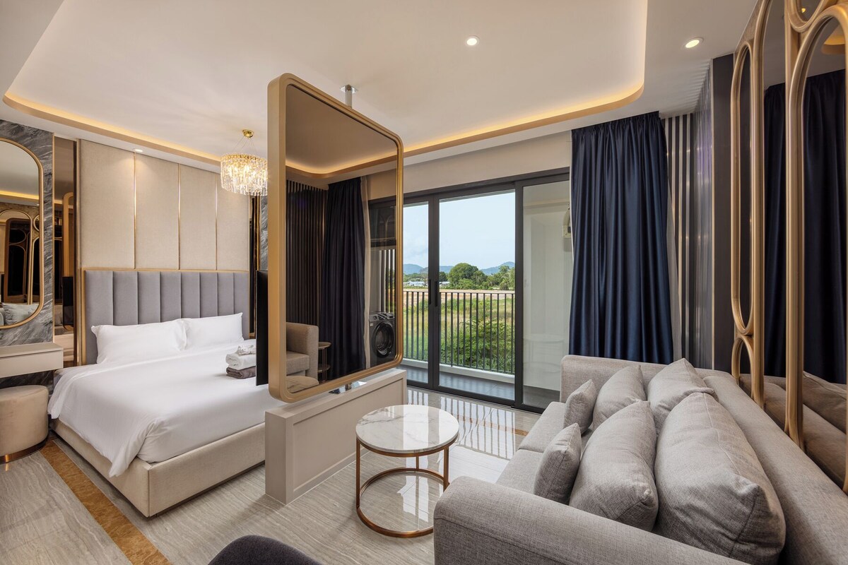 Una habitación de hotel moderna con una cama grande, un sofá, una mesita, un espejo y un balcón con vistas.