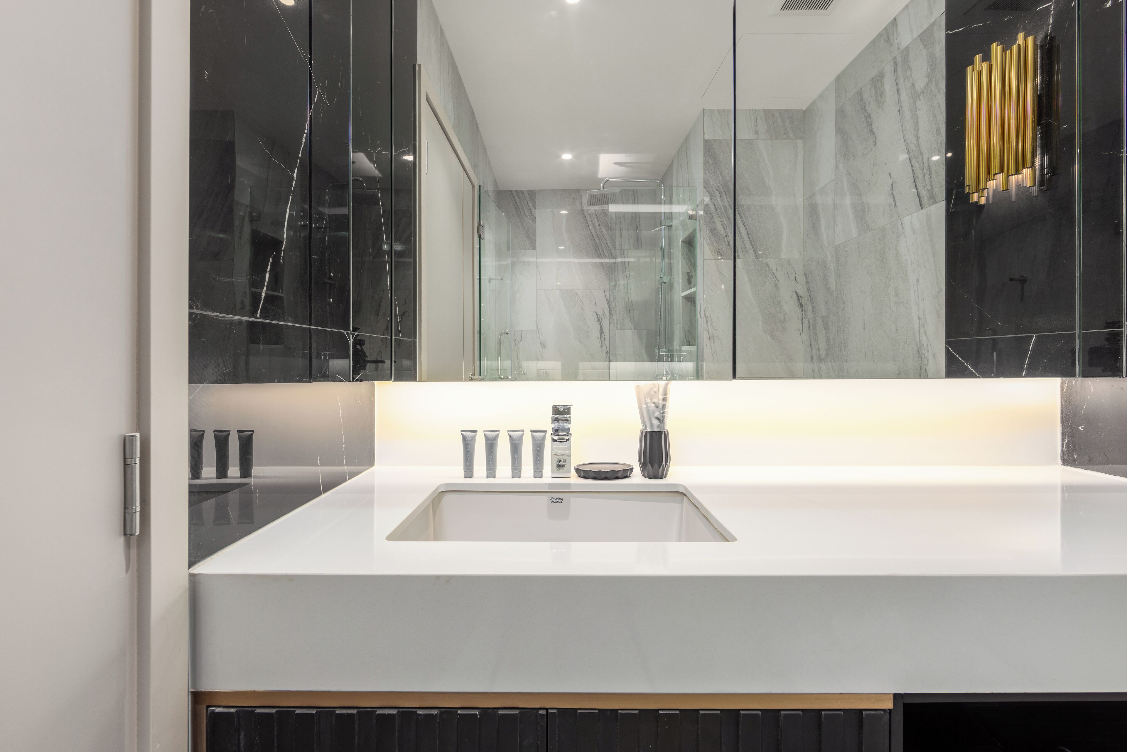 A modern bathroom with a large mirror, white countertop, and a glass shower enclosure.