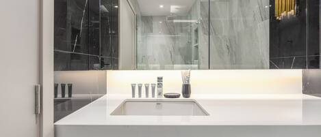 A modern bathroom with a large mirror, white countertop, and a glass shower enclosure.