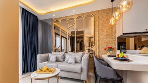 A modern living room with a grey sofa, a round coffee table, and a kitchen area with a white countertop and bar stools. - Bellevue Lagoon Premium Apart Hotel (Choeng Thale)