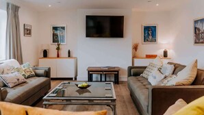 A modern living room with a sofa, a coffee table, and a TV mounted on the wall. - Modern Country Escape for 12 Guests -Rural Setting (Llanarthney)