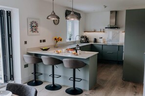 A modern kitchen with a central island, bar stools, pendant lights, and a window providing natural light.