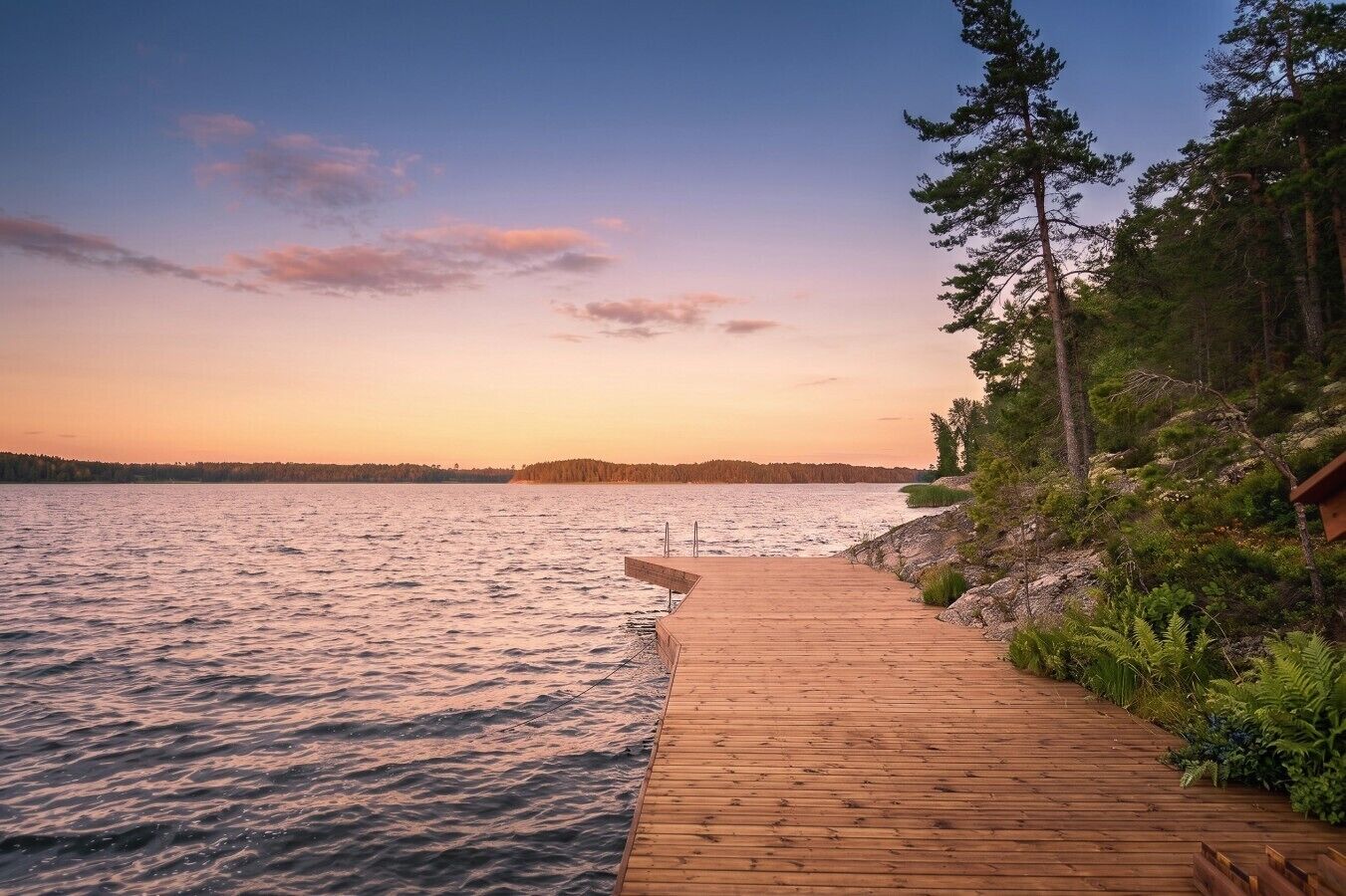 A wooden dock extending into a body of water, surrounded by trees and a clear sky.