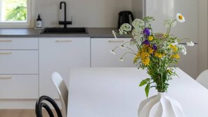 Een moderne keuken met witte kasten, een zwarte hanglamp en een bloemenvaas op tafel.