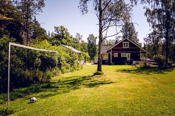 A house with a red exterior, a porch with outdoor seating, and a grassy yard with a soccer goal.