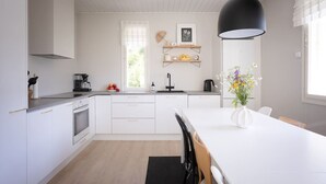 Een moderne keuken met witte kastjes, een zwarte hanglamp en een eethoek met een witte tafel en stoelen.
