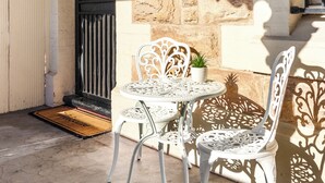 Un patio con un muro de piedra, un portón negro y una mesa y sillas de metal blanco.
