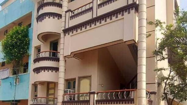 A multi-story residential building with balconies, a tiled driveway, and a neighboring blue building. - AER Residency (Tiruvannamalai)