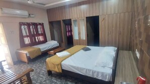 A hotel room with two single beds, a wooden wardrobe, and a bench. - AER Residency (Tiruvannamalai)