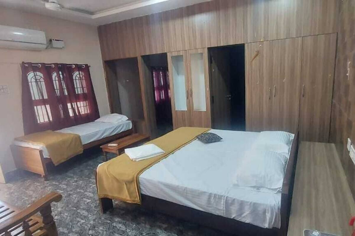 A hotel room with two single beds, a wooden wardrobe, and a bench.