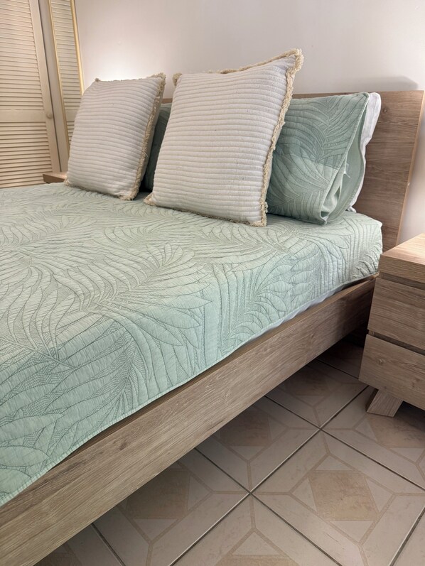 A bed with a quilted leaf-patterned bedspread, two pillows, and a wooden headboard.