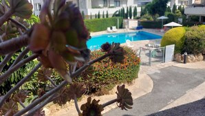 A modern building with a pool, surrounded by greenery and a clear sky. - 1st Class Pool View Apt. (Paphos)