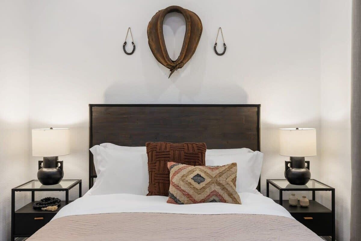 A neatly made bed with two pillows, a dark headboard, and two bedside tables with lamps.
