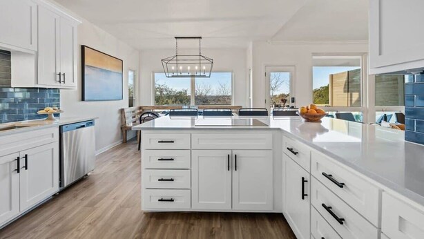 Una cocina moderna con armarios blancos, una isla central y un amplio ventanal que proporciona luz natural.