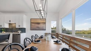 Una cocina moderna con armarios blancos, una mesa de comedor de madera para seis personas y un amplio ventanal con vistas al exterior.