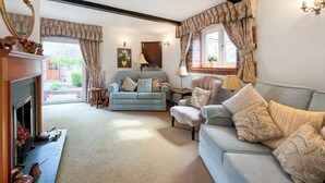 A cozy living room with a fireplace, two sofas, a table, and a window with curtains. - Henfaes Bach - UK50268 (Nannerch, near Clwydian Range)