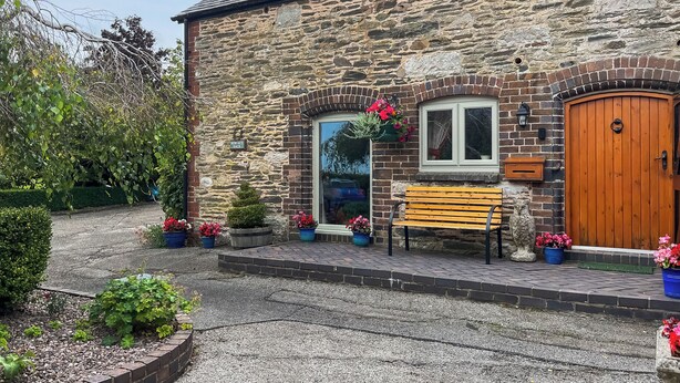A stone building with a wooden door, a bench, and potted plants. - Henfaes Bach - UK50268 (Nannerch, near Clwydian Range)