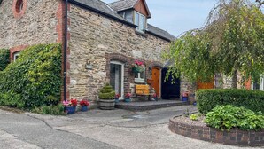 A stone building with a traditional design, featuring a stone facade, a wooden door, and a small porch with potted plants. - Henfaes Bach - UK50268 (Nannerch, near Clwydian Range)