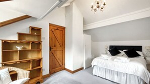 A bedroom with a large bed, a wooden wardrobe, a wicker chair, and a chandelier. - Henfaes Bach - UK50268 (Nannerch, near Clwydian Range)