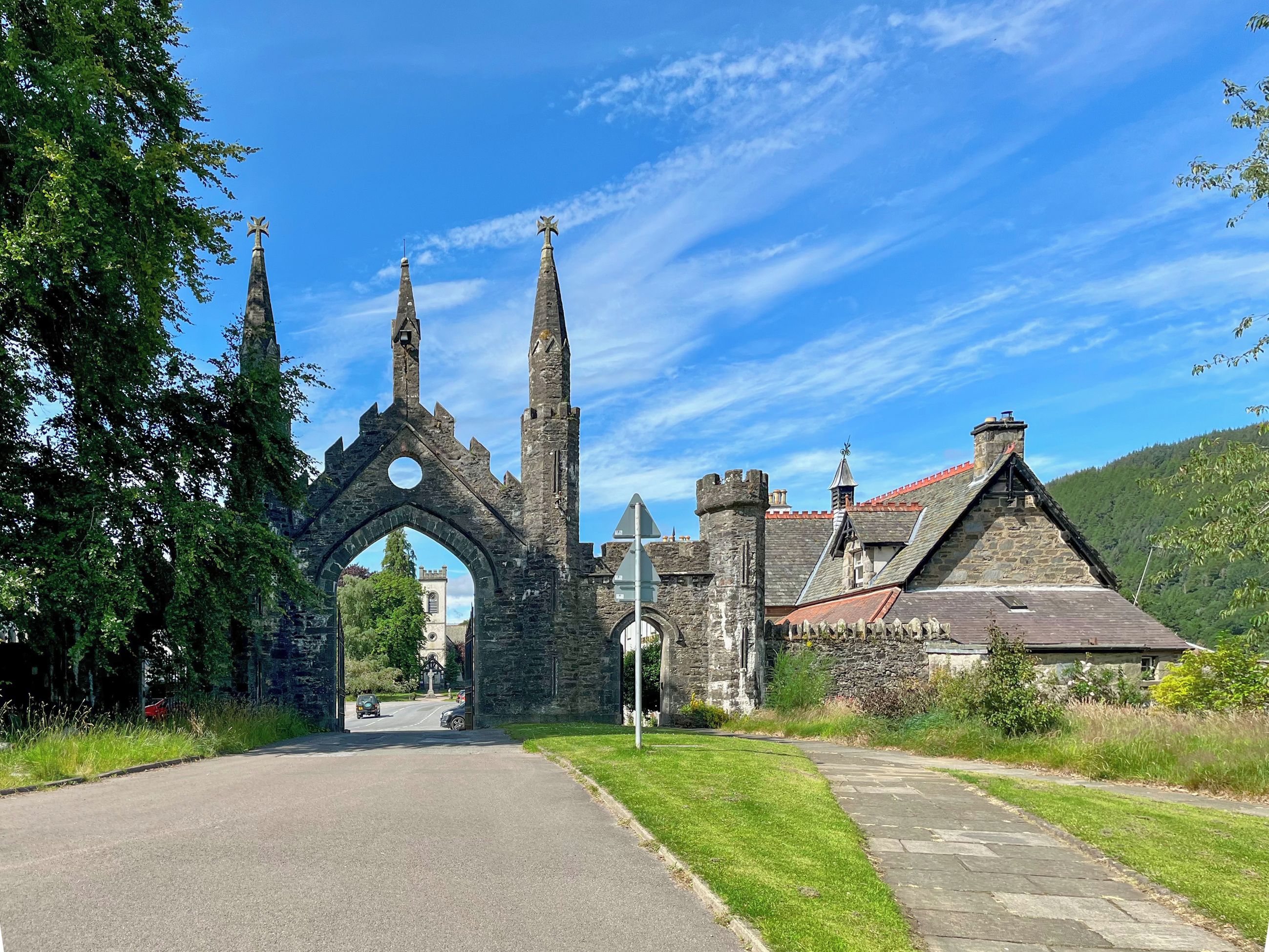 A historic stone archway leading to a castle-like building with multiple towers and a red-tiled roof.