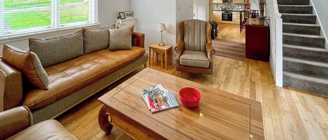 Una sala de estar moderna con un sofá de cuero, una mesa de centro de madera y una silla. Una escalera conduce a un nivel superior.