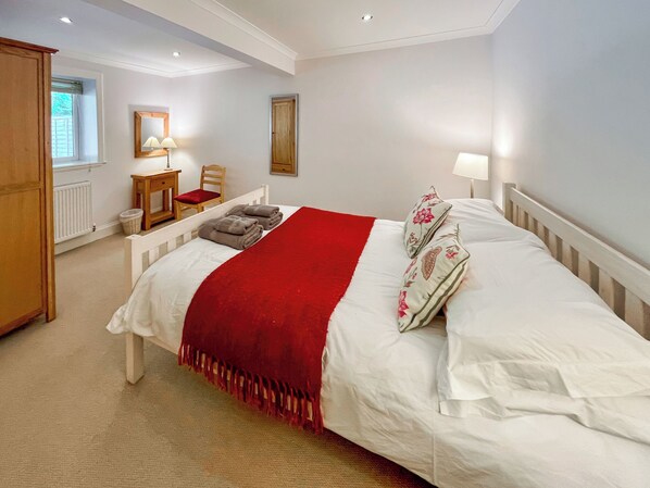 Un dormitorio ordenado con una cama grande, una silla, una mesita con lámpara y un radiador.