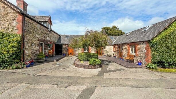 A courtyard with stone buildings, a central garden, and a bench. - Henfaes Bwthyn - UK50266 (Nannerch, near Clwydian Range)
