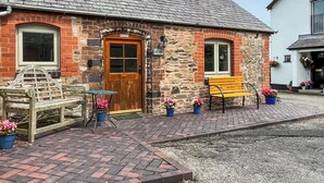 A stone building with a wooden door and windows, a bench, and potted plants. - Henfaes Bwthyn - UK50266 (Nannerch, near Clwydian Range)
