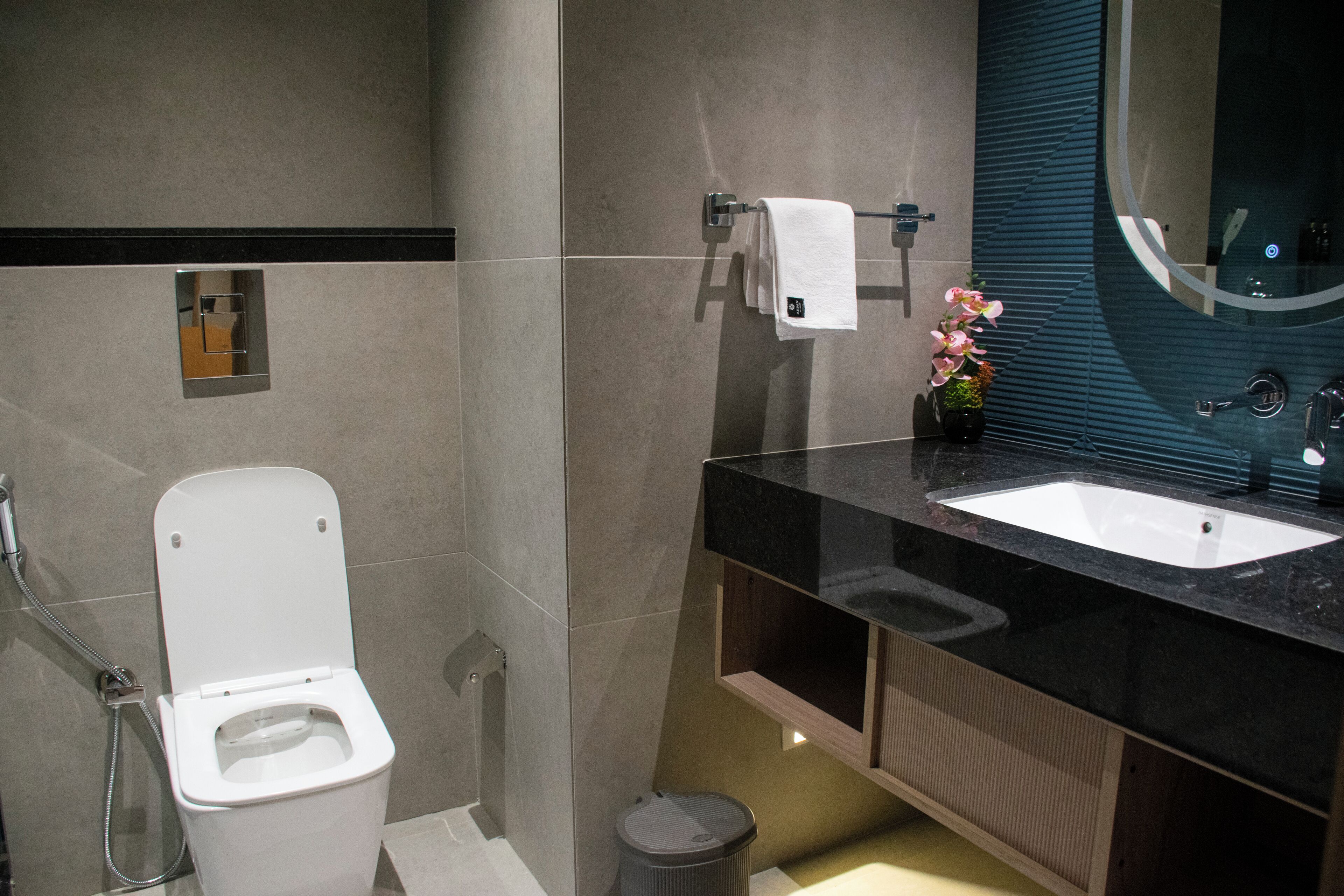 Un baño moderno con inodoro blanco, lavamanos negro y un espejo.