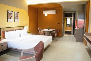 Una habitación de hotel con una cama, un escritorio y una silla. Hay una planta en el escritorio y un marco de fotos en la pared.