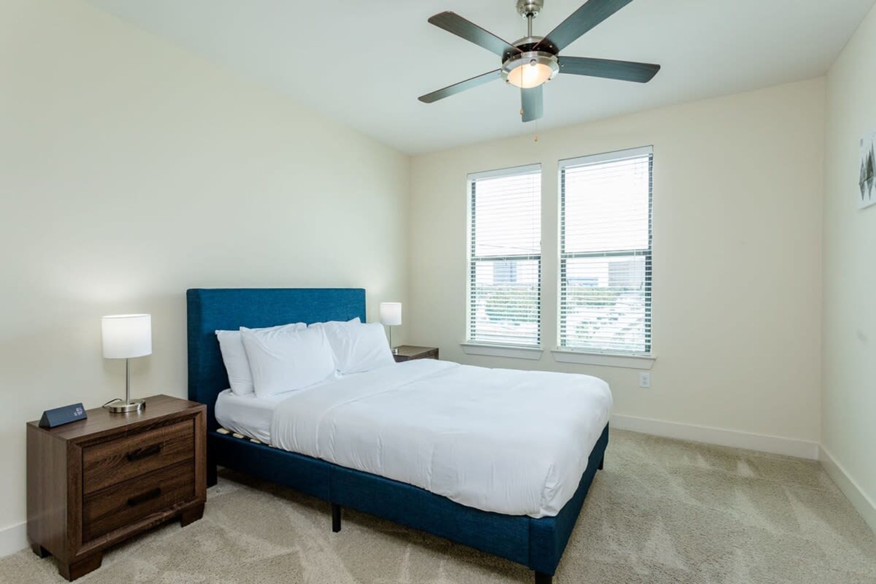 A bedroom with a bed, nightstands, a ceiling fan, and a window with blinds.