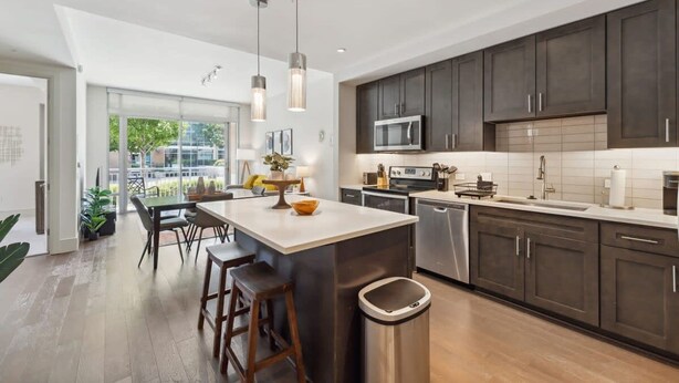 A modern kitchen with dark cabinets, stainless steel appliances, and a central island with stools. - The Preston Charm I Premium 1BR in Dallas (Dallas)