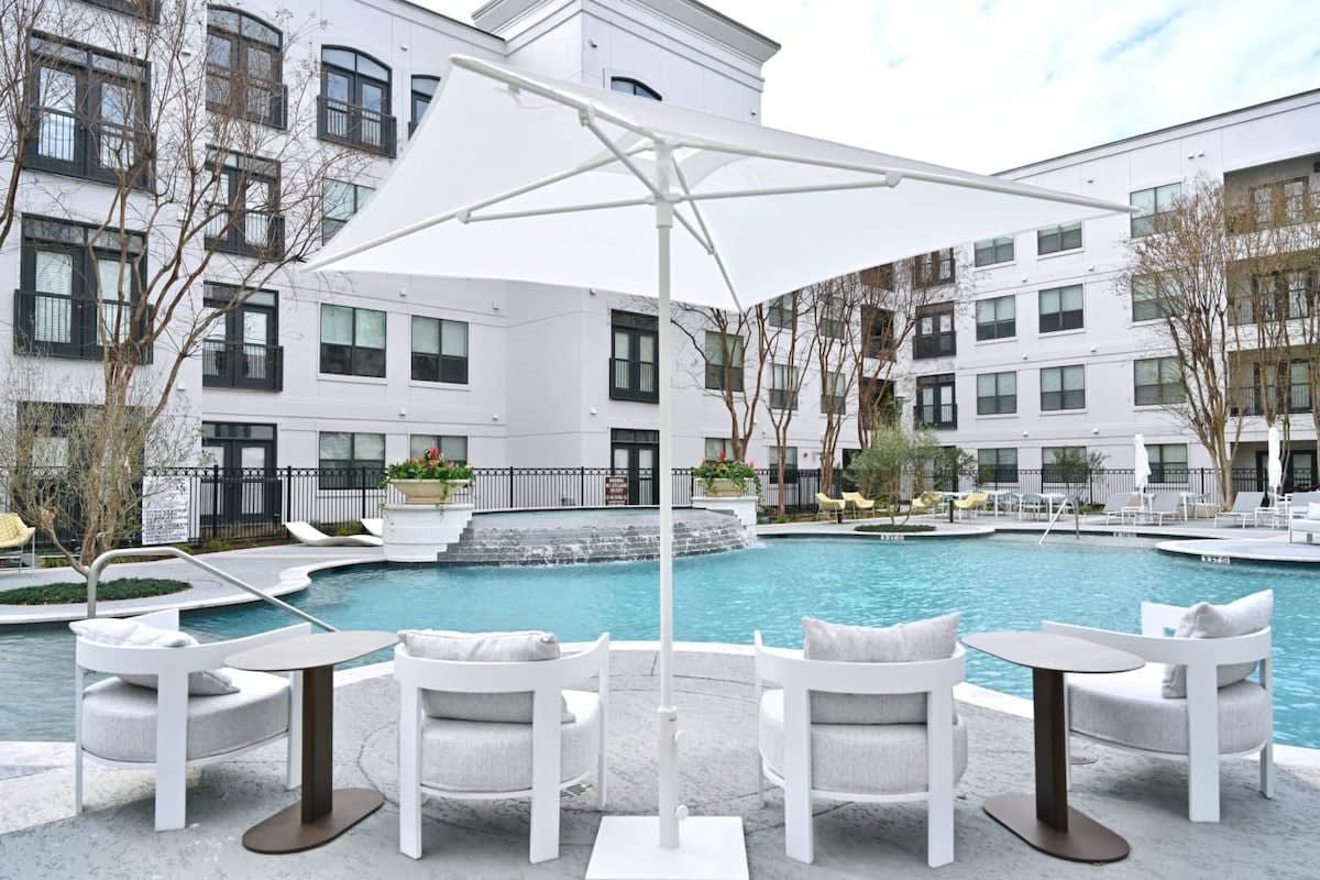A poolside area with white outdoor furniture, a white umbrella, and a building with multiple windows in the background.