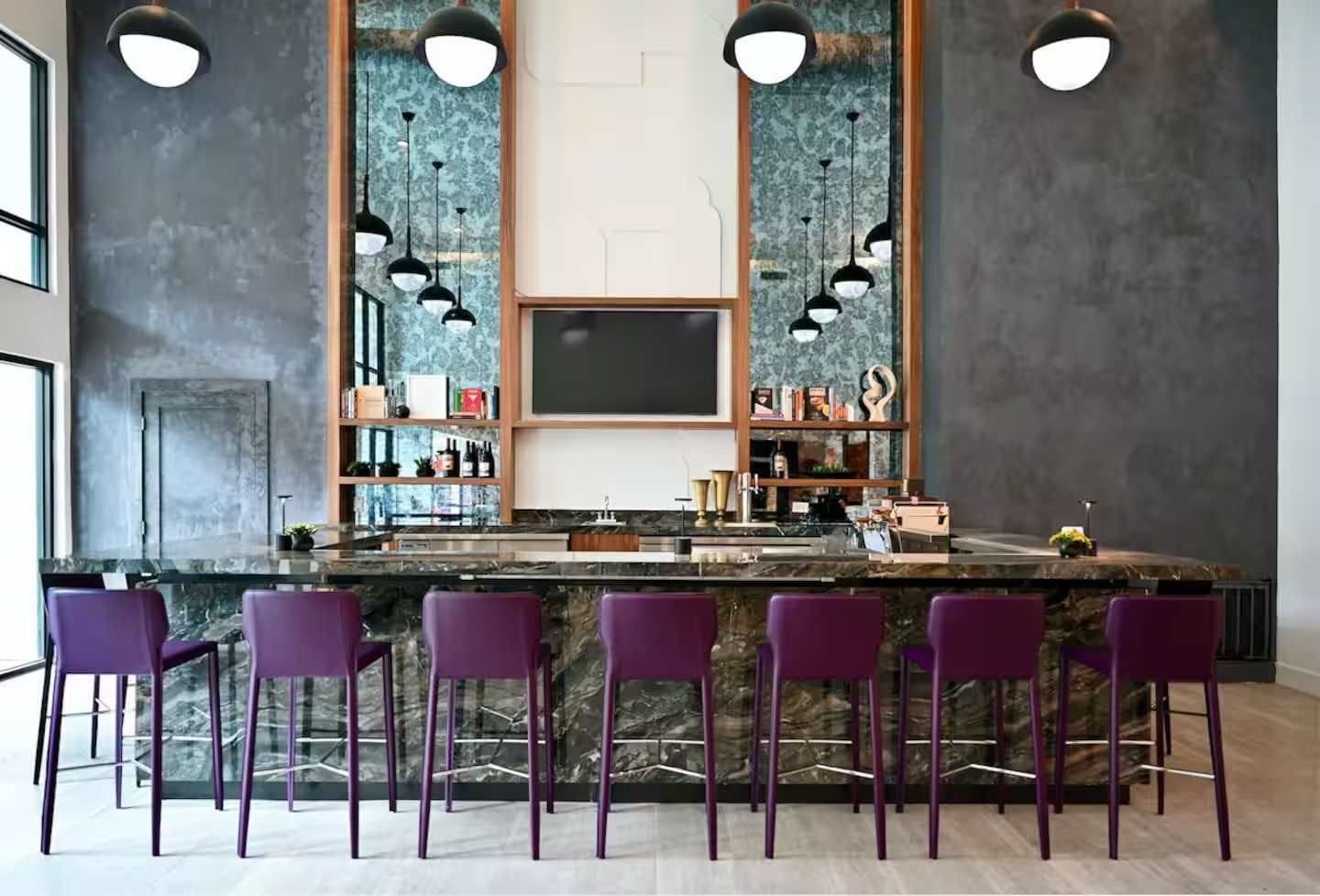 A bar area with a marble countertop, purple bar stools, and pendant lighting.