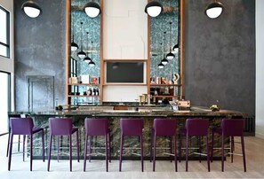 Zona de bar con mostrador de mármol, taburetes morados e iluminación colgante.