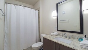 Un baño con cortina de ducha, inodoro, lavabo con espejo y toallero.
