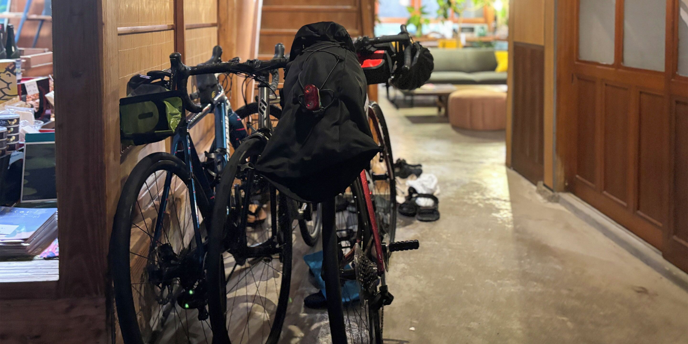 A narrow hallway with bicycles parked against the wall, a wooden door, and a small seating area with a cushion.