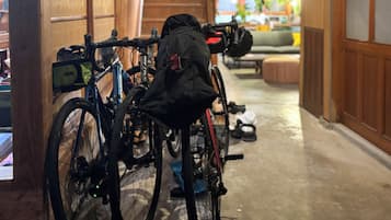 A narrow hallway with bicycles parked against the wall, a wooden door, and a small seating area with a cushion.