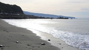 A beach with a rocky shoreline and a distant view of a forested hill. - junos (Nahari)