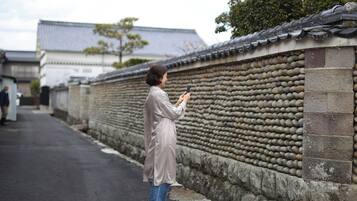 A person standing on a street next to a traditional stone wall with a tiled roof.