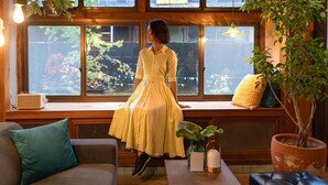 A woman in a yellow dress sitting on a bench by a window with a view of greenery. - junos (Nahari)