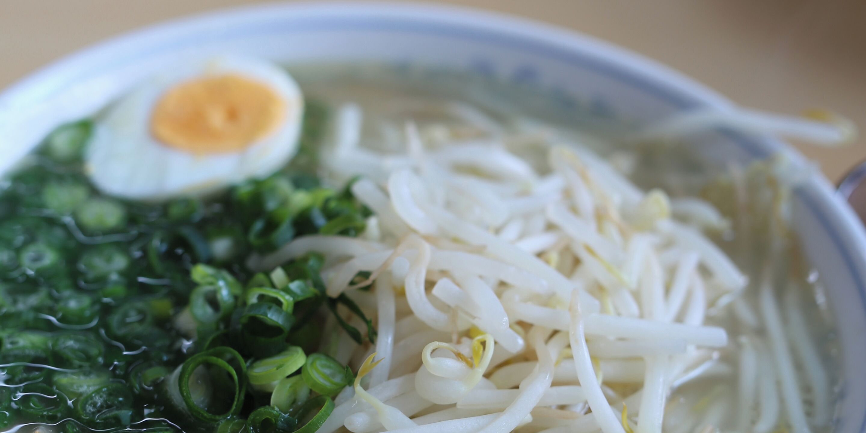 A bowl of noodle soup with sliced green onions and a half-boiled egg.