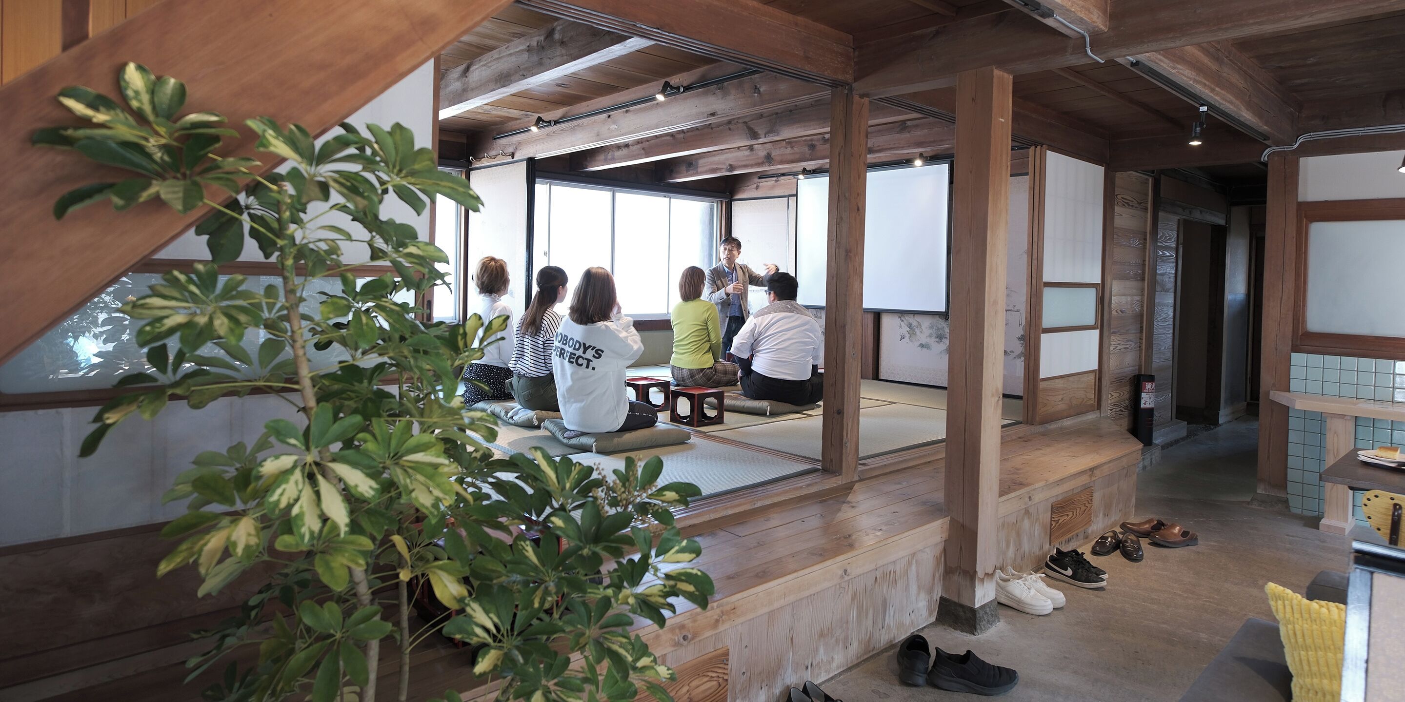 A room with wooden beams, tatami mats, and a group of people sitting in a circle.