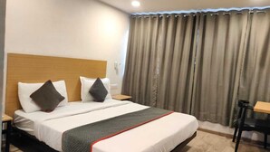 A hotel room with a bed, a wooden headboard, a desk, and a window with curtains.