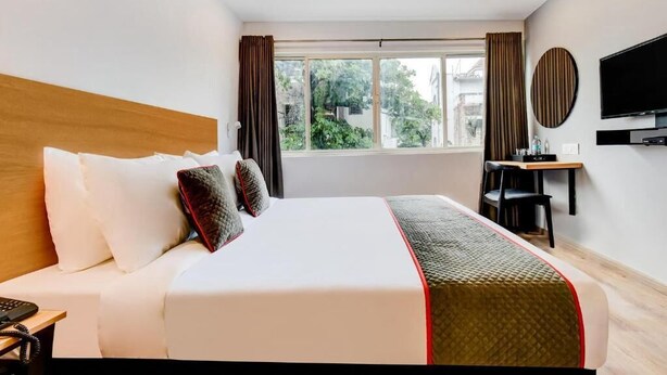 A hotel room with a large bed, a desk, a television, and a window with curtains.