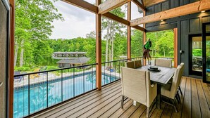 A wooden deck with a pool view, outdoor seating, and a glass door leading to a covered area.
